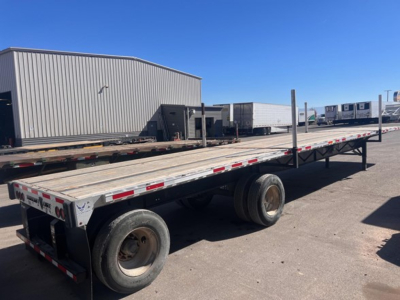 Transcraft spread air combo flatbed trailer with dual rear axles and wooden deck, parked in lot under clear sky.
