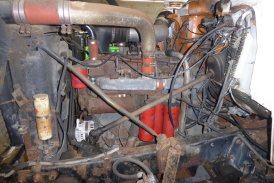 Engine bay of a 1985 Mack R690T cab and chassis showing exposed hoses, wiring, and components including air intake piping, coolant hoses, and engine block.