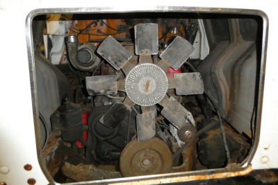 Mack R690T engine bay showing clutch/flywheel and belt-driven fan with radiator shroud and surrounding components.