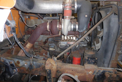 Mack R690T cab and chassis engine bay showing turbocharger, intake piping, radiator fan, and rusted frame crossmember.
