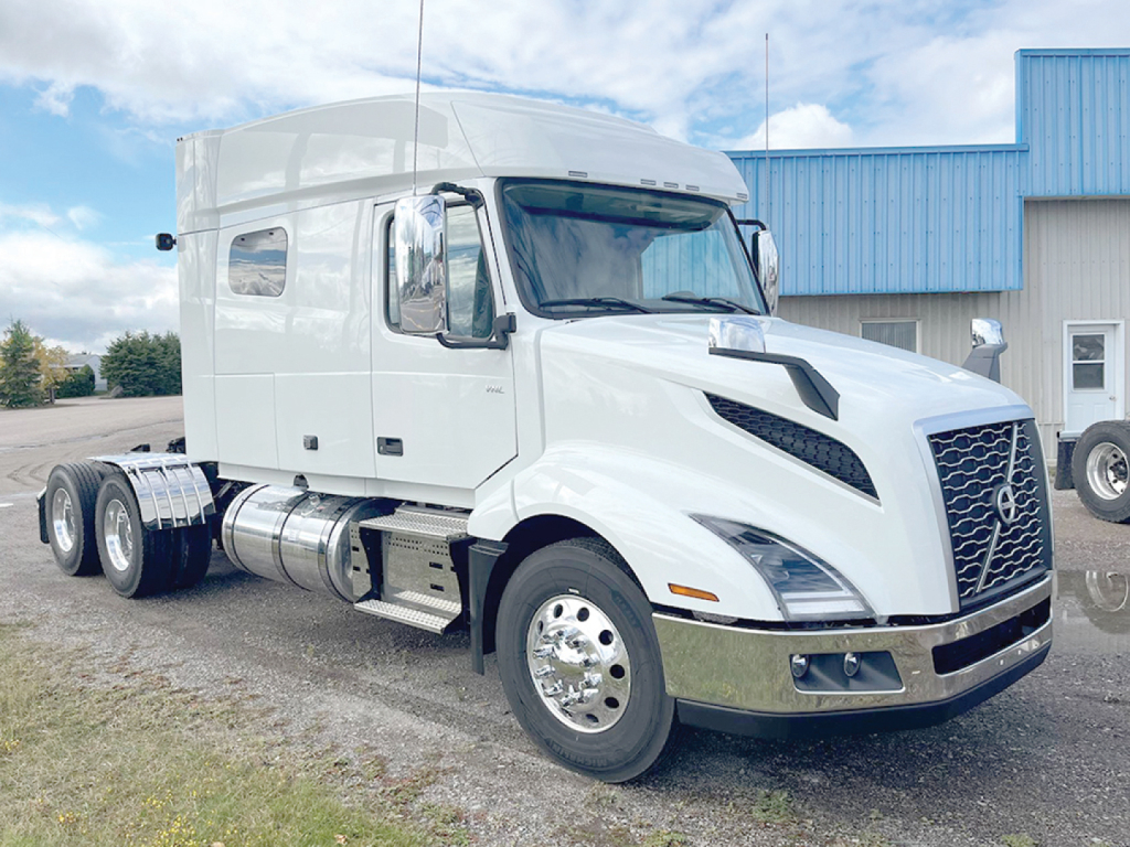 Truck cab side view showing Volvo VNL 740 sleeper with chrome fuel tanks and dual rear axles.