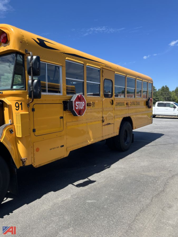 Yellow 2015 Blue Bird Vision school bus side view showing door, stop sign, windows, and partial bus lettering.