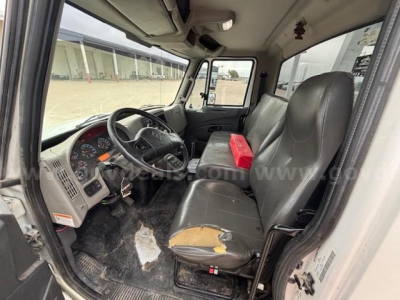 Truck cab interior showing steering wheel, dashboard, driver seat with torn upholstery, passenger seat, and center console; plastic dashboard with gauges visible.