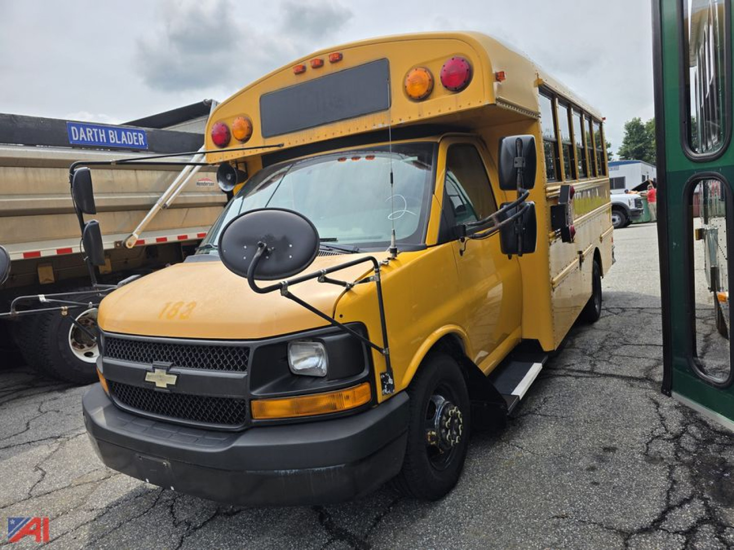 Chevrolet Express school bus front-left view with amber body, black bumper, and round mirrors.