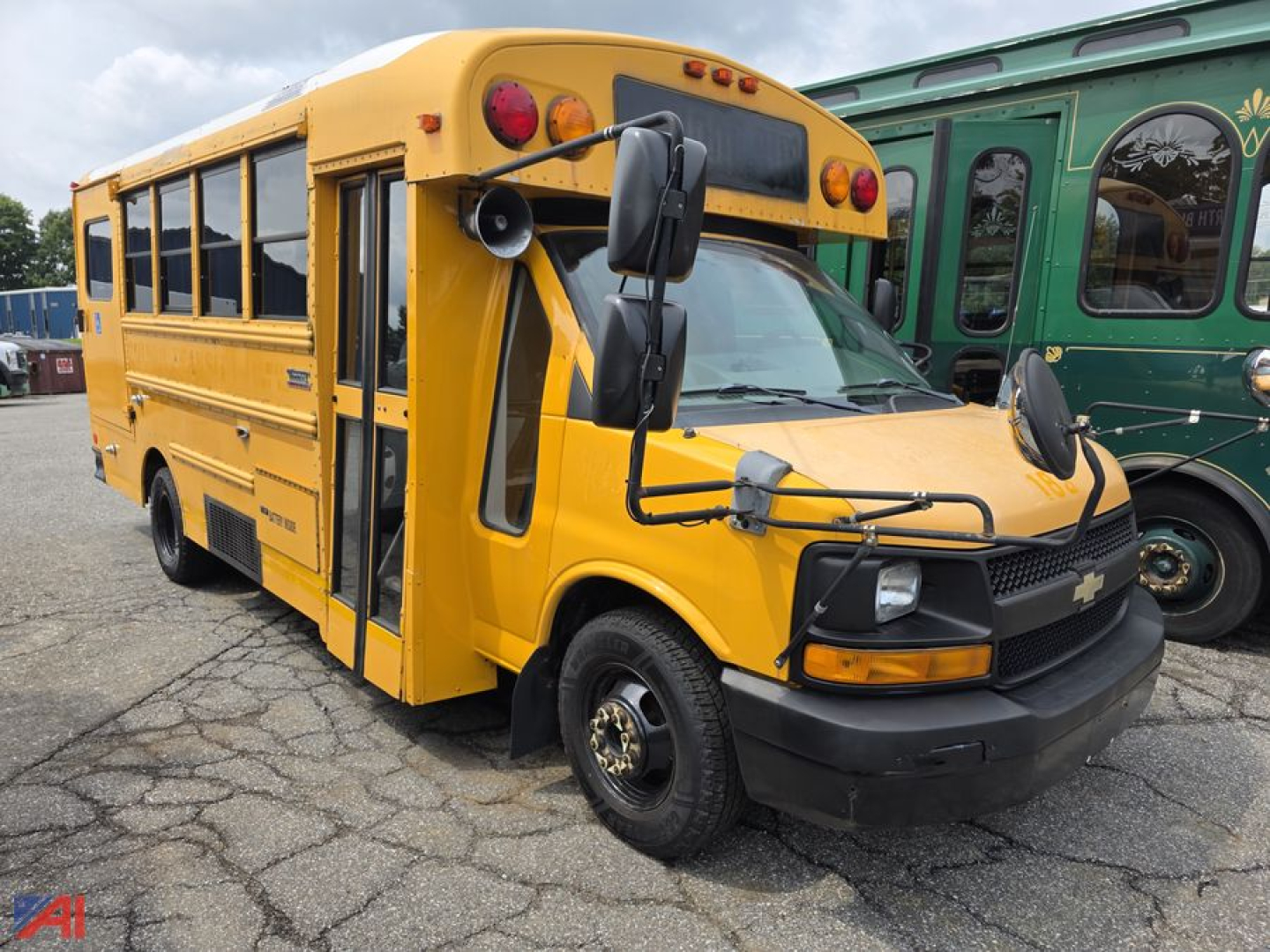 Yellow school bus in driveway, front-left view, Chevrolet logo on grille, extended mirrors, black bumper, side windows