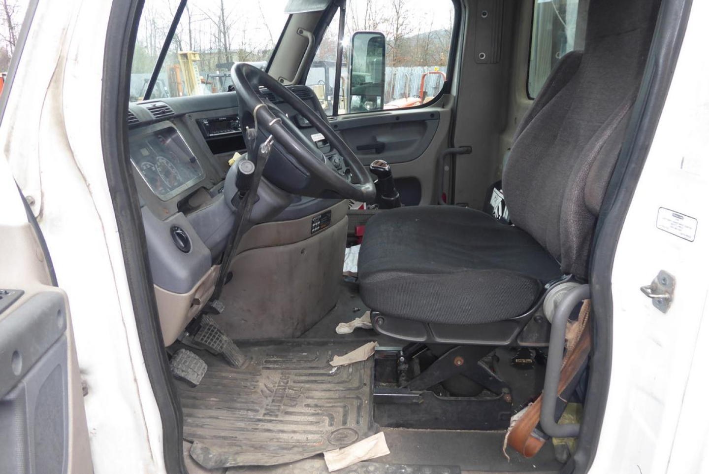 Cab interior of 2012 Freightliner Cascadia 113 daycab showing steering wheel, driver seat, dashboard, and entry door.