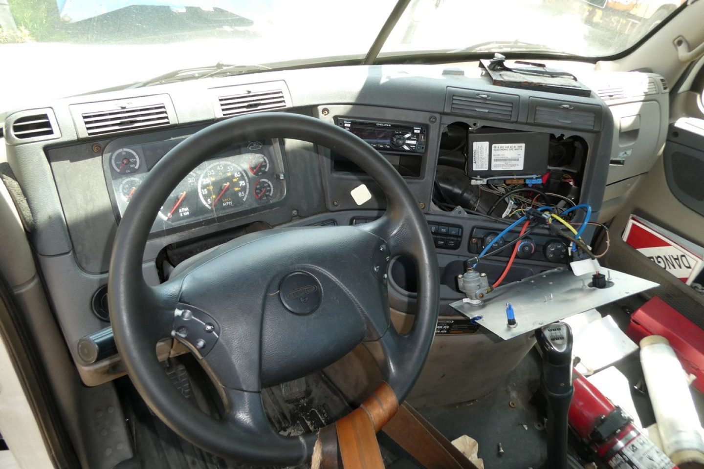 Cab interior of a Freightliner Cascadia truck showing dashboard, steering wheel, exposed wiring, and a partially disassembled center console.
