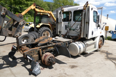 Truck cab and exposed drivetrain components in a yard with other equipment; 2012 Freightliner Cascadia 113 listed as used.