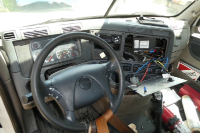 Cab interior of a Freightliner Cascadia truck showing dashboard, steering wheel, exposed wiring, and a partially disassembled center console.