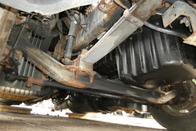 Underbody view of a Freightliner Cascadia 113 truck showing drivetrain and suspension components with rust on metal parts and black oil pan.