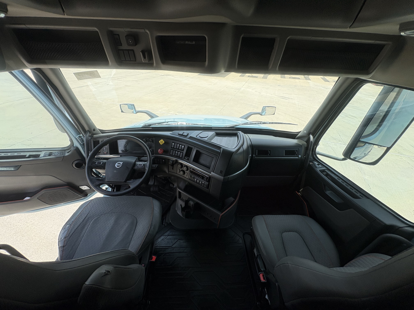 Cab interior of a Volvo VNL truck showcasing steering wheel, dashboard, and front seats from driver’s perspective.