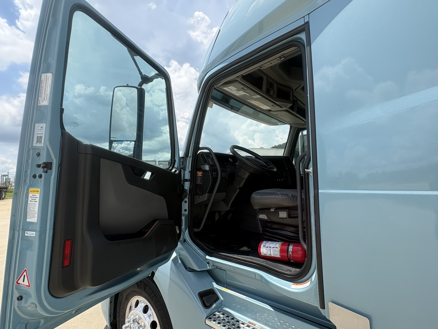 Volvo VNL64T760 truck cab with door open showing steering column and interior; side view of the cab in blue.