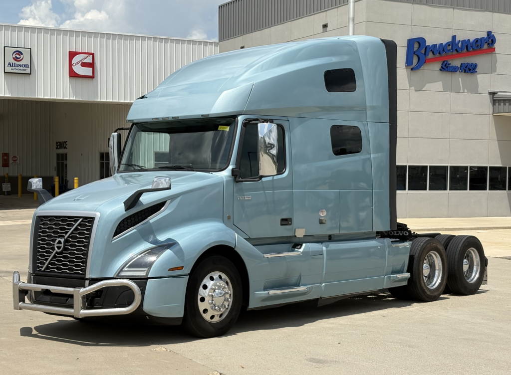 Volvo VNL64T760 sleeper cab truck in light blue, three-quarter front view, showing grille, headlights, dual rear axles, and side windows.