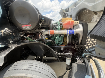 Volvo VNL64T760 engine bay view with label stickers and hoses; visible components include air filter canister, coolant reservoir (orange cap), colored hoses, and engine block.