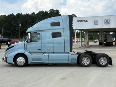Volvo VNL64T760 sleeper cab truck in light blue, side view, shows tandem rear axles and service building in background.