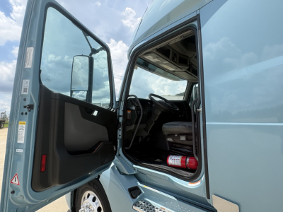 Volvo VNL64T760 truck cab with door open showing steering column and interior; side view of the cab in blue.