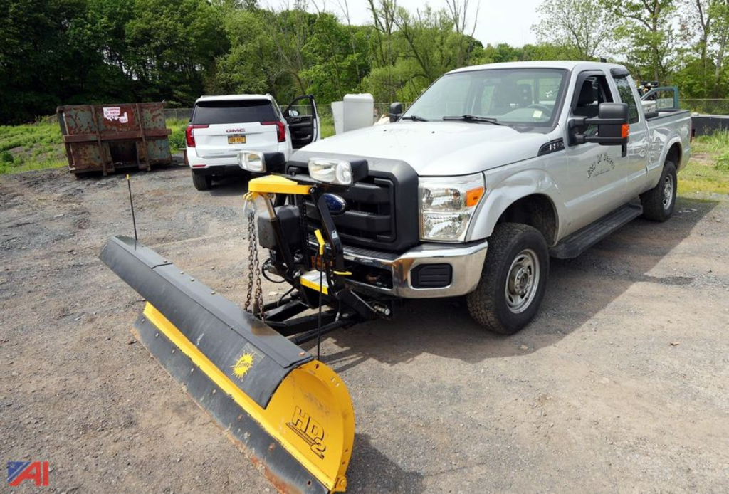 Ford F-250 pickup with front mounted snow plow attachment in a gravel lot.
