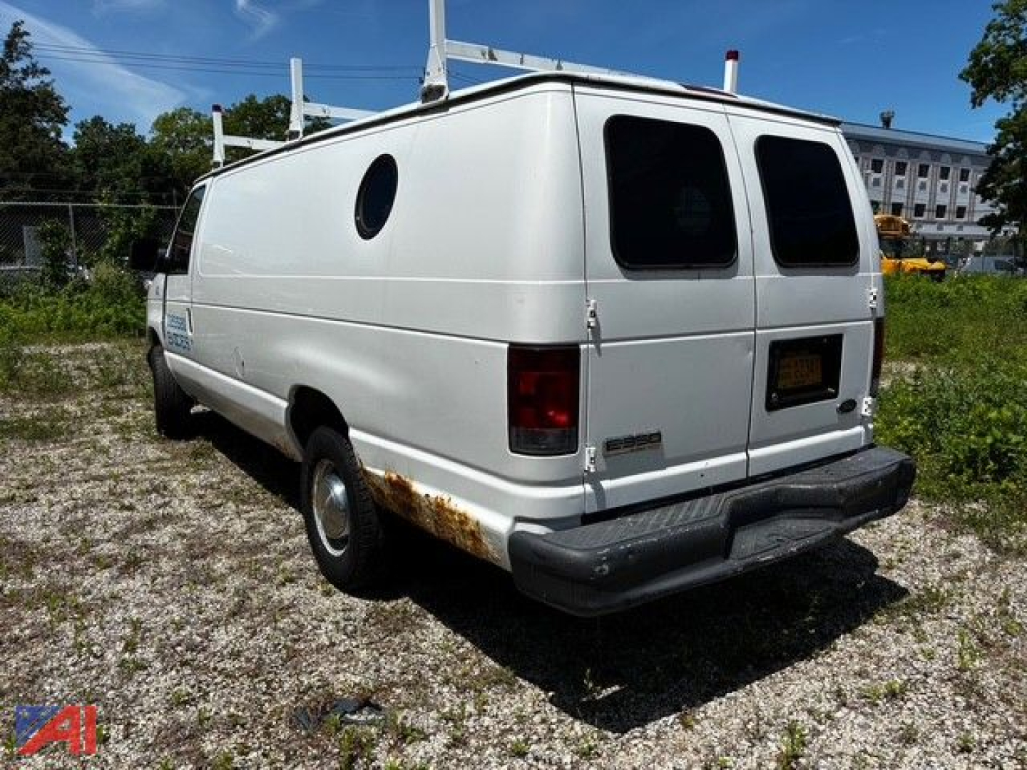 Ford E-350 cargo van rear-left view with circular side window and rust near wheel arch.