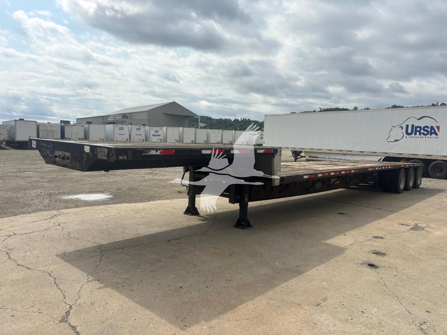 Flatbed trailer in yard showing extended drop deck with two axle configuration and front landing gear.