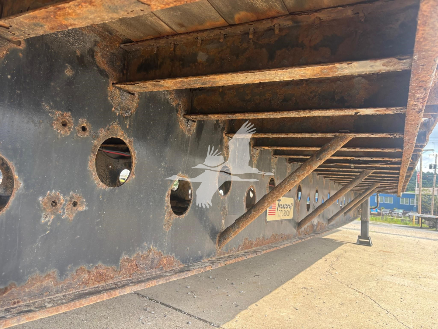 Underbelly of a Transcraft DTl-3000 trailer showing structural crossmembers and circular cutouts with rust-colored framing.