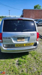 Rear view of a silver 2014 Dodge Grand Caravan with license plate and yellow school vehicle sign.