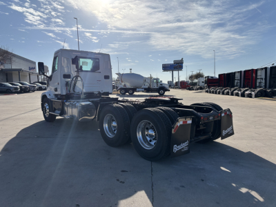 Truck chassis with tandem rear axles and white cab, view from left side showing fifth wheel mounting, wheels, and fuel tanks.