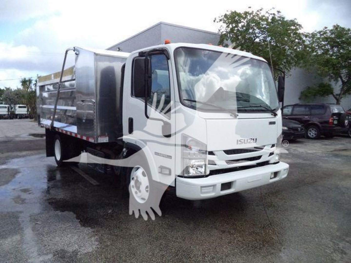 Isuzu NPR XD dump truck in a parking lot, white cab with silver dump bed, front view angled left. Visible text includes 'ISUZU' on grille.