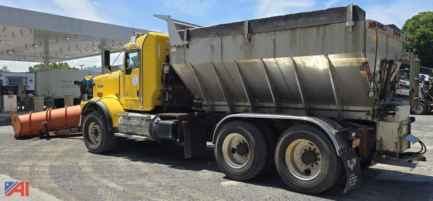 Kenworth T800 dump truck with a large steel dump bed and plow attachment at the front, yellow cab and chassis, multiple rear axles.