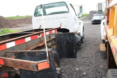 Truck cab and chassis with lifted white cab, trailer hitch, and debris; equipment on a dirt surface with a yellow vehicle nearby.
