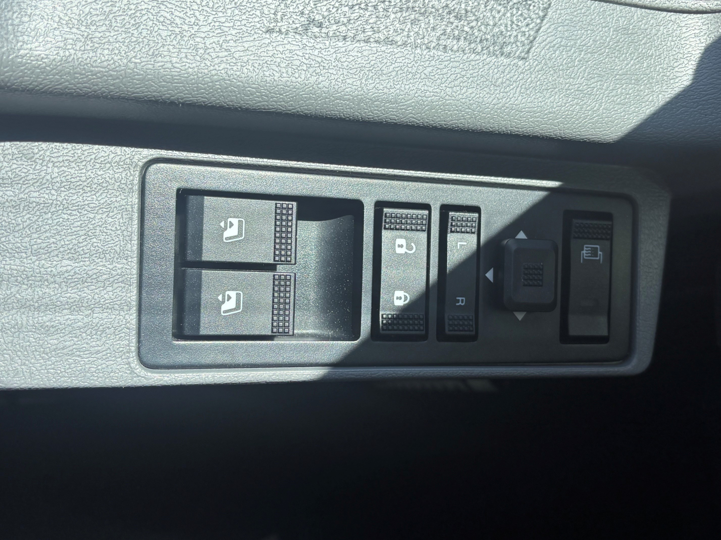 Panel of control switches in a Mack GR64B truck showing window/lock controls and buttons. Visible text/icons on switches.