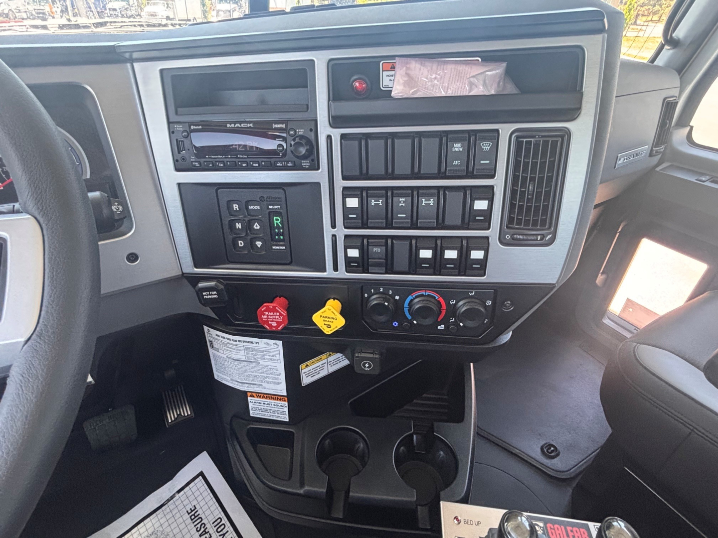 Mack GR64B dash area showing steering wheel, radio, control switches, climate controls, and cup holders.