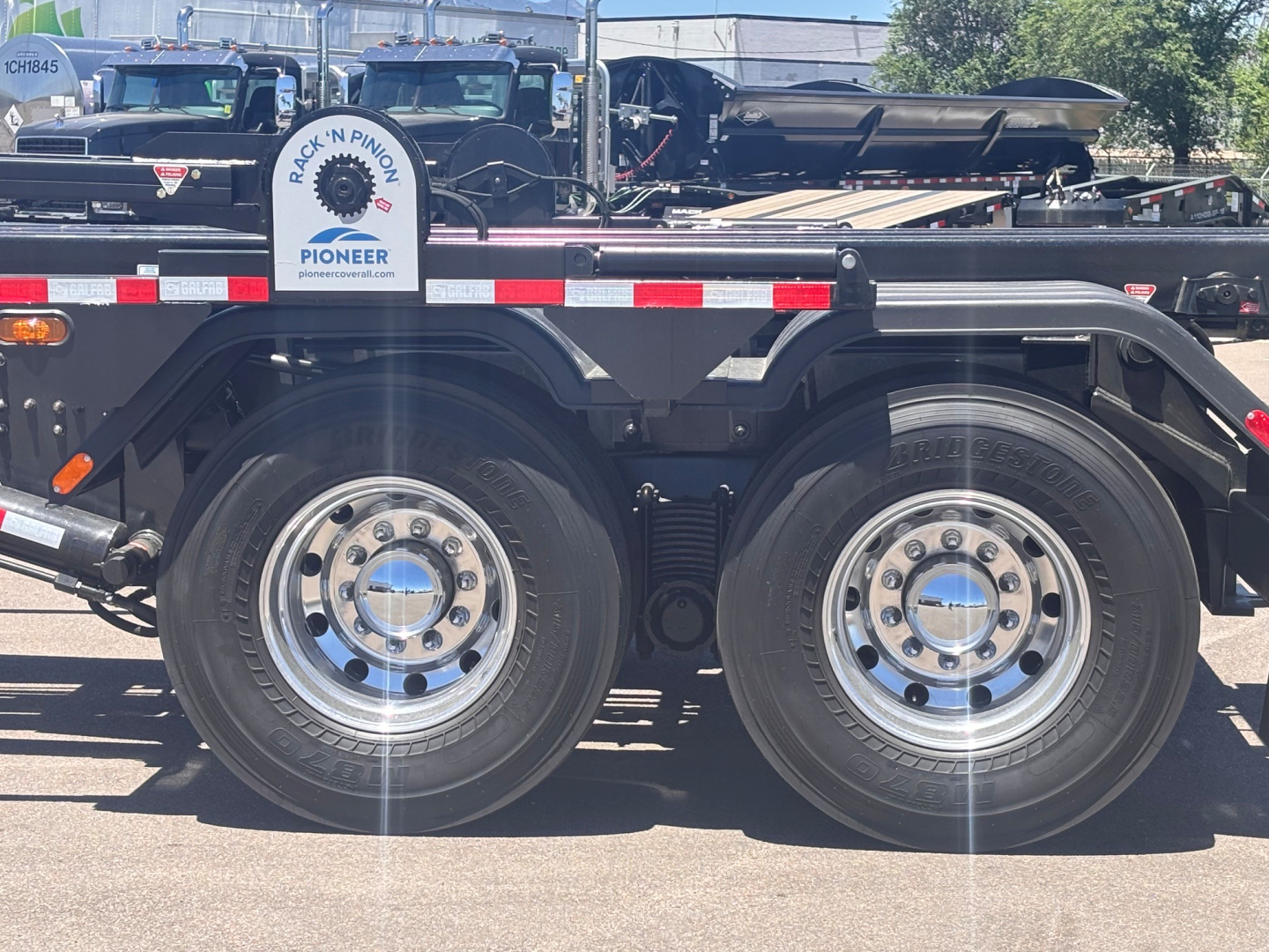 Mack GR64B rolloff truck wheel area with dual rear axles, metal frame, and chrome hubcaps visible.