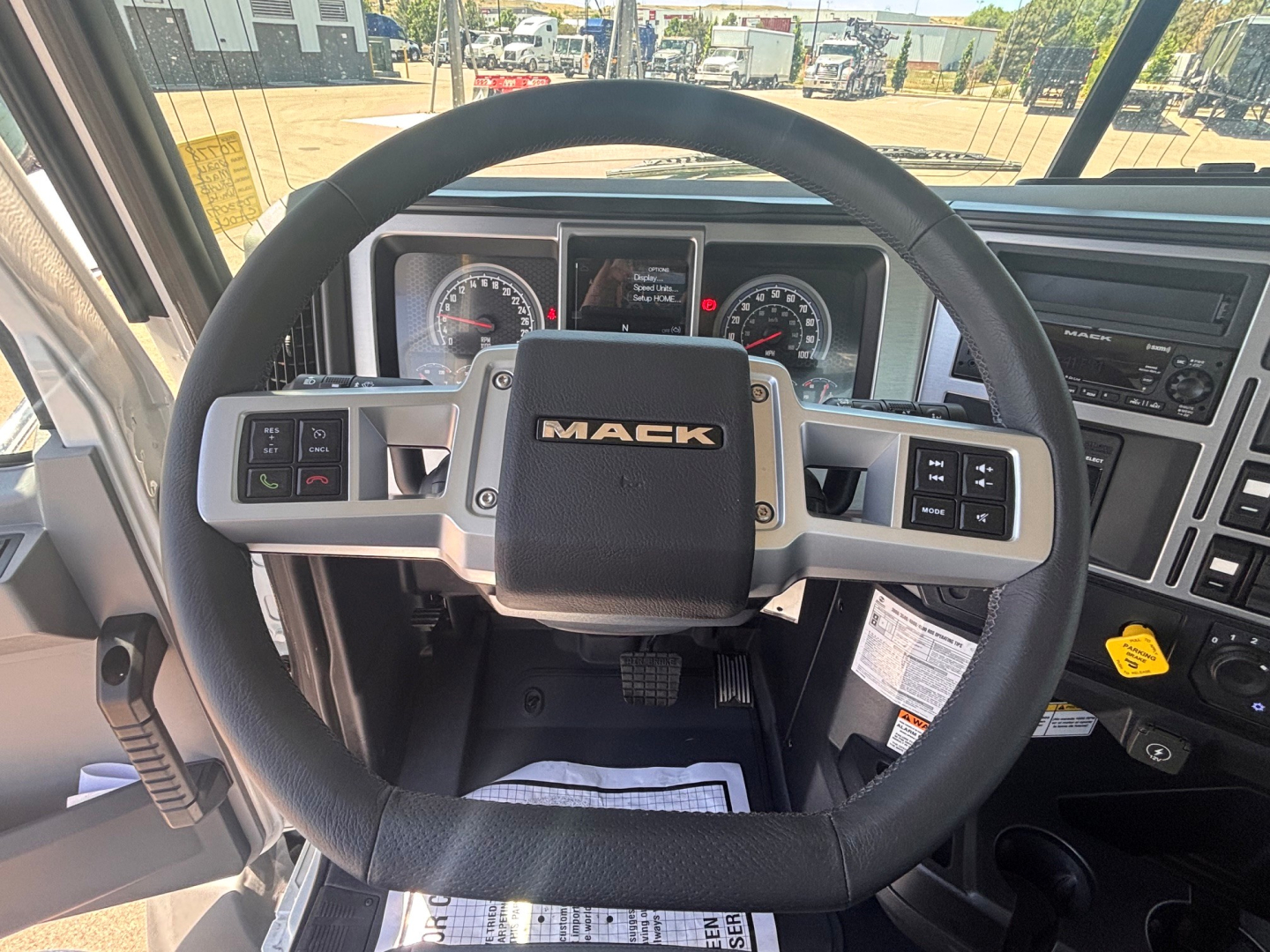 Steering wheel and instrument cluster of a new Mack GR64B truck showing the Mack logo on the steering wheel and dashboard controls.