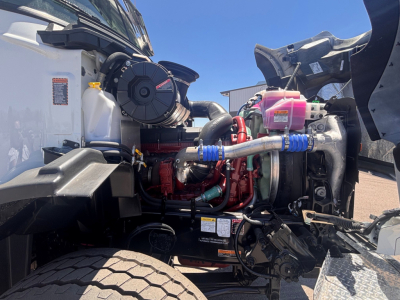 Truck engine bay of a 2026 Mack GR64B showing engine with red components, hoses, coolant reservoir, and turbo assembly.
