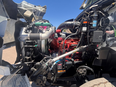 Mack GR64B engine bay view showing red diesel engine, hoses, radiator, and various components visible.