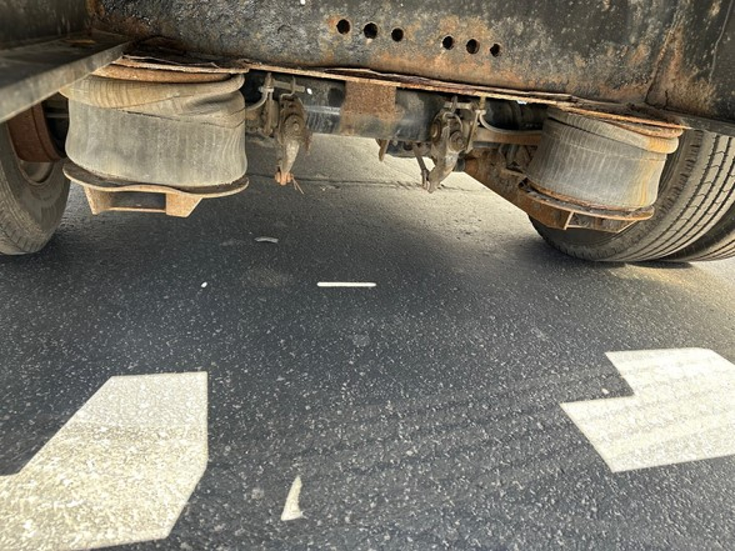 Underbody view of a used 2013 Transcraft trailer with dual axles and air suspension, showing wheels, leaf springs, and ballast; some rust and road grime on the frame.