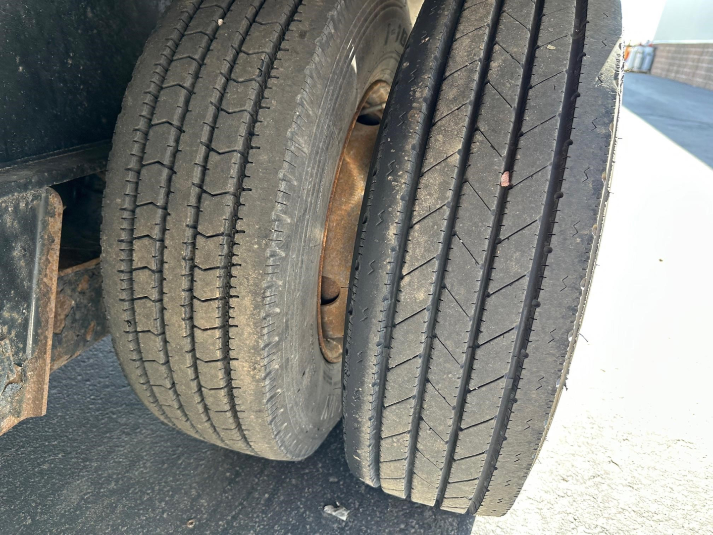 Dual rear tires of a Transcraft drop deck trailer with visible tread patterns and rusted wheel hubs.