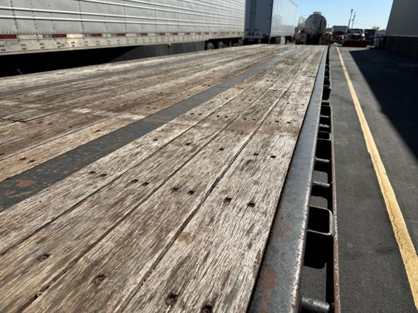 Trailer bed showing weathered wooden deck with metal stake pockets along edge; perspective from front of drop deck trailer.