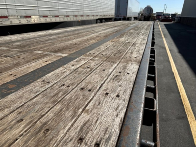 Trailer bed showing weathered wooden deck with metal stake pockets along edge; perspective from front of drop deck trailer.