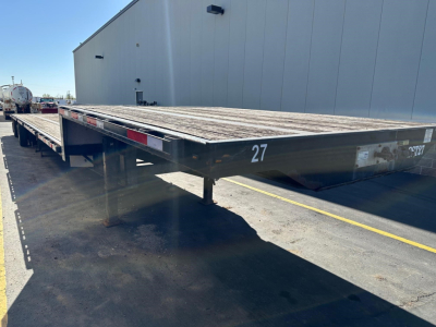 Transcraft steel drop deck trailer showing flatbed with weathered deck and white markings; number 27 on front edge; side rails and support legs visible.