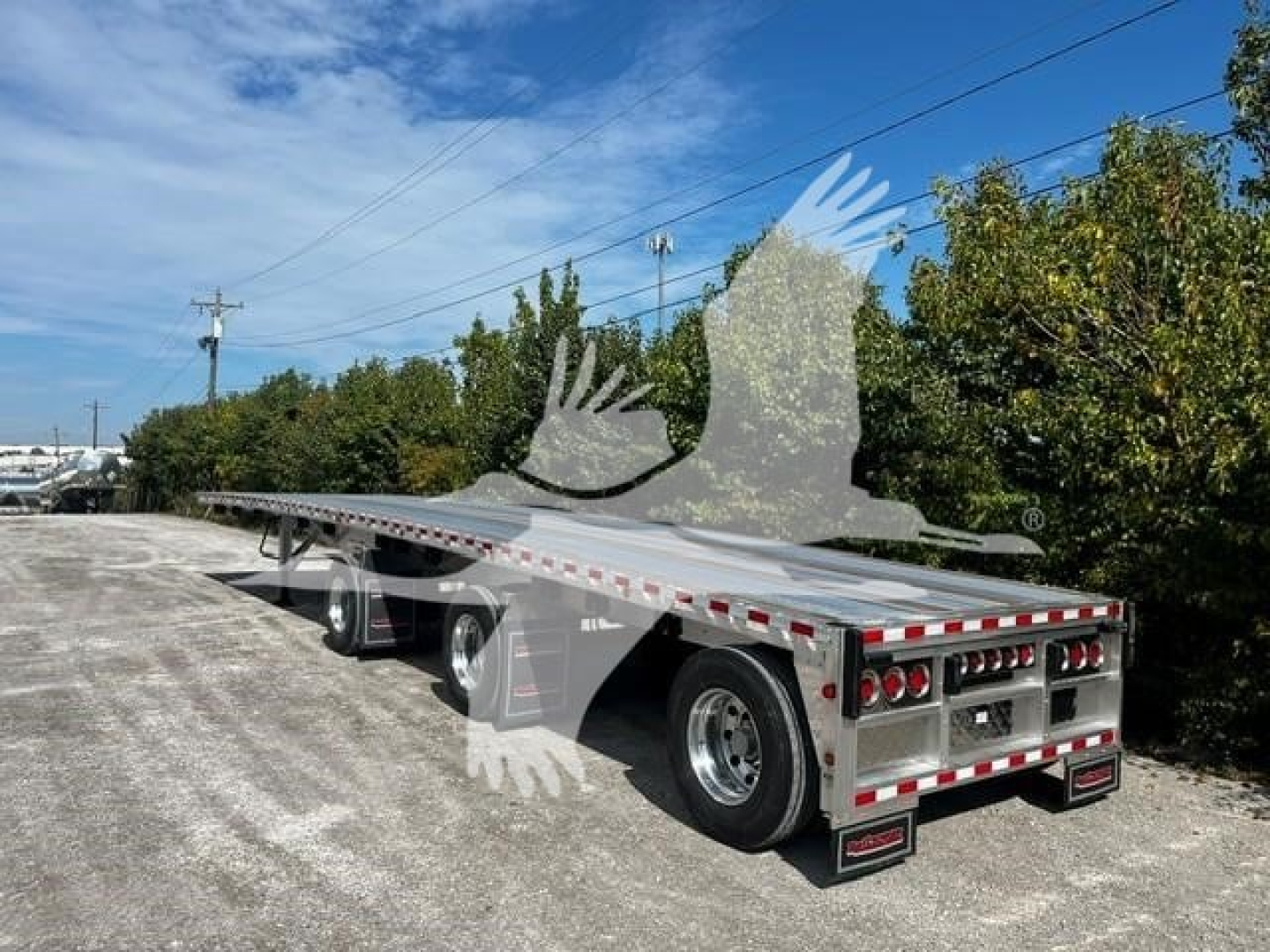 Flatbed trailer showing extended deck and dual rear axles with chrome wheels and reflective red/white safety stripes.