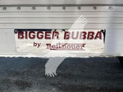 Flatbed trailer rear showing 'BIGGER BUBBA' plaque by Reitnouer with riveted aluminum body and shadowed ground; license area not visible.