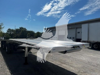 Flatbed trailer showing aluminum deck and tandem axles with black tires, in-service outdoor storage.