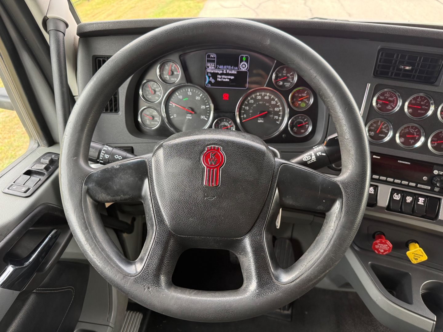 Kenworth T680 truck cockpit showing steering wheel and gauge cluster with digital display and various knobs.