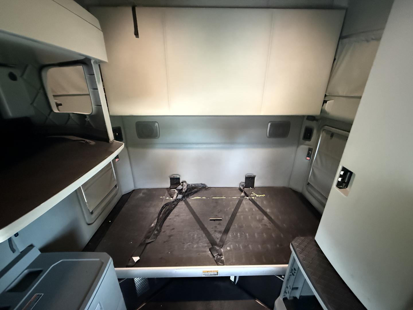 Kenworth T680 sleeper cab interior cargo area with side storage compartments and dual strap anchors on the floor.