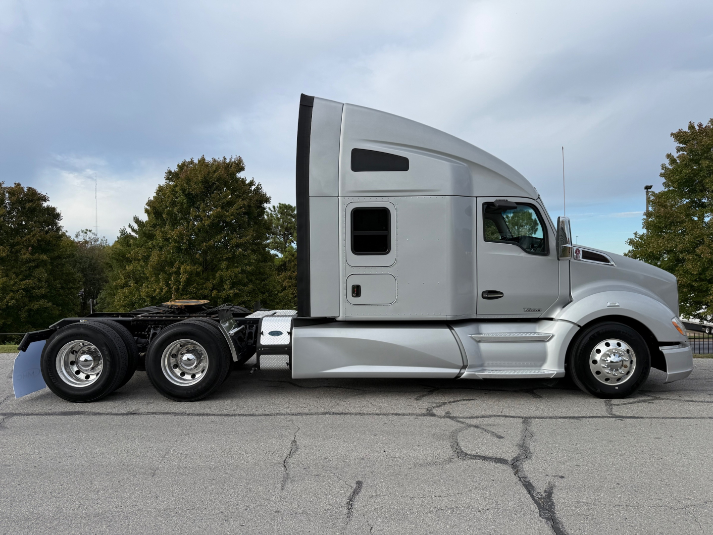 Kenworth T680 tractor side profile with sleeper cab, silver paint, three rear axles, visible wheels, minimal text on cab window area.