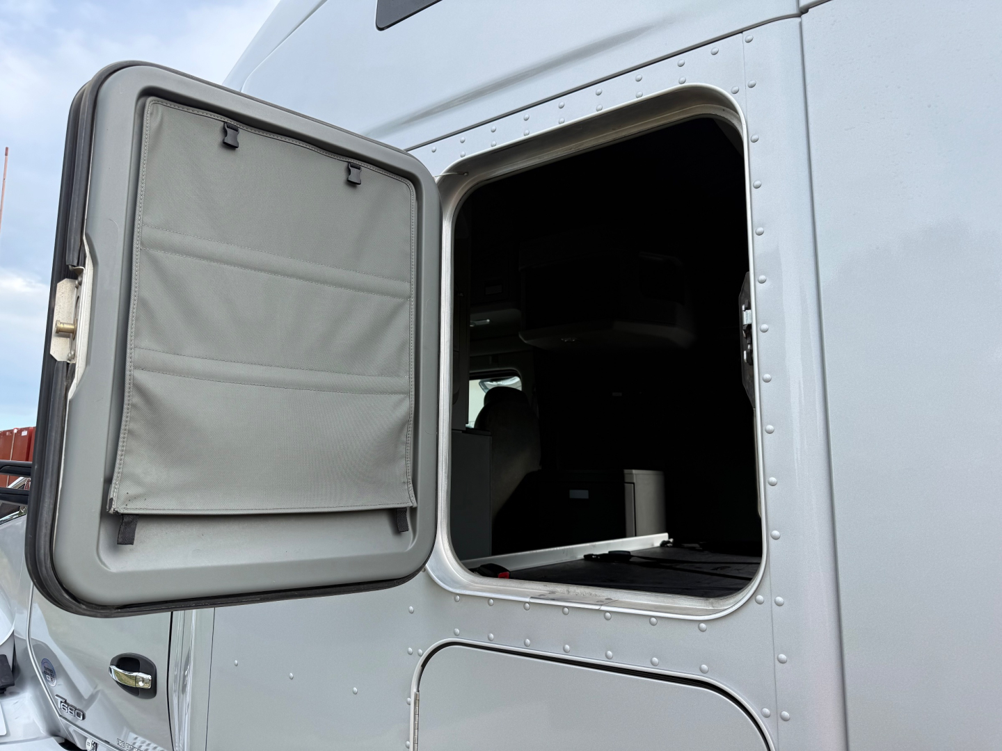 Kenworth T680 truck sleeper cab door open showing interior window frame and cargo area.