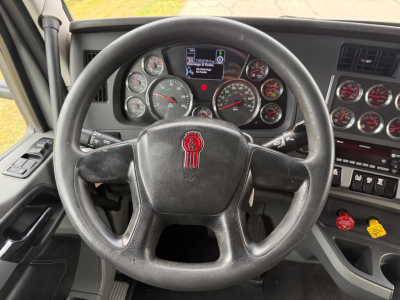 Kenworth T680 truck cockpit showing steering wheel and gauge cluster with digital display and various knobs.