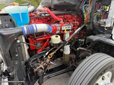 Kenworth T680 engine bay showing XD15 engine with red components, blue coolant reservoir, hoses, and front axle area.