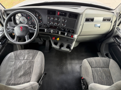 Kenworth T680 interior dashboard and front seats from driver’s perspective with steering wheel, gauge cluster, center console, and pedals.